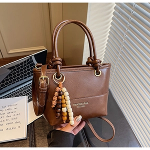Detail of coffee brown bucket bag with knot handle and wooden bead charm on its side