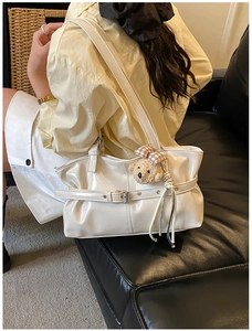 Detail of white glossy leather tote bag with pleats, silver buckles and cute plush bear charm