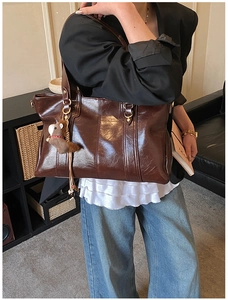 Dettaglio di una borsa tote marrone scuro vintage con texture lucida e ciondolo orso