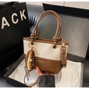 Detail of two-tone bucket bag in white and brown with beaded charm and gift packaging