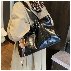 Dettaglio della borsa tote in pelle nera lucida con anelli dorati e charm a cavallo