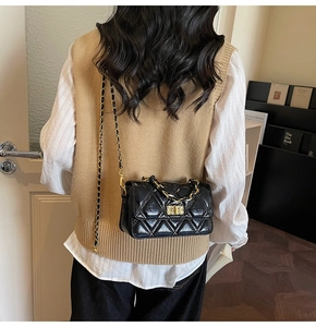 Détail d'un sac bandoulière noir matelassé avec chaîne dorée porté par un mannequin