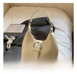 Détail du sac hobo beige avec boucle argentée posé sur une veste de costume grise