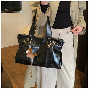 Dettaglio della borsa tote nera lucida con fibbia dorata e ciondolo a forma di cavallo