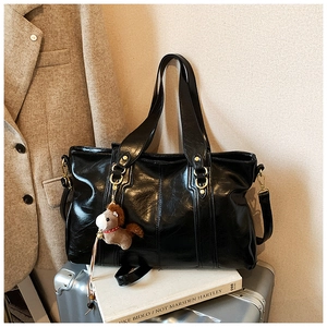 Dettaglio di una borsa tote nera in pelle cerata con finiture dorate e ciondolo