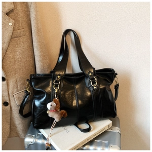 Dettaglio di una borsa tote nera grande con pelle lucida e ciondolo a forma di cavallo