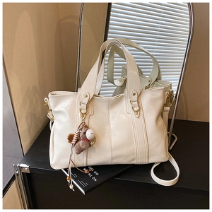 Dettaglio della borsa tote in pelle bianco crema con cuciture, hardware oro e ciondolo