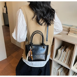 Model wearing a black glossy leather bucket bag with a retro beaded charm in a home setting