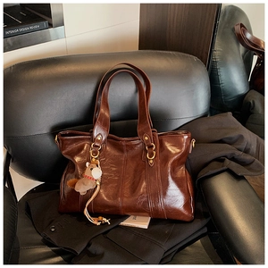 Dettaglio borsa tote in pelle marrone lucida con anelli dorati e ciondolo a cavallo
