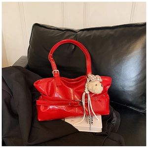 Detail of red patent leather tote with metal eyelets and a plush bear charm on a dark sofa