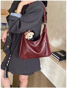 Détail du sac Hobo en cuir brillant rouge foncé avec bandoulière à nœud et ours peluche