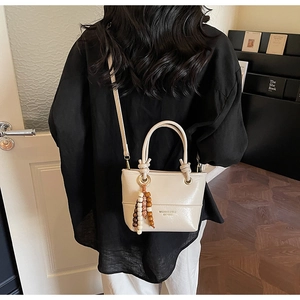 Detail view of cream bucket bag with beaded tassel and shoulder strap on a model