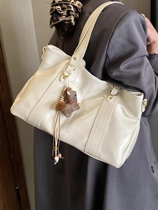 Borsa tote grande bianco crema con cuciture e ciondolo a cavallo su cappotto grigio