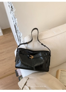 Detailed close-up of glossy black leather shoulder bag with vintage gold metal twist lock