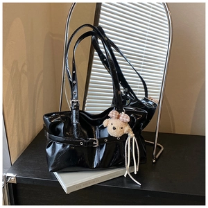 Detail of black glossy leather tote bag with metallic buckles and plush dog charm