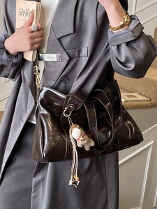 Borsa tote in pelle marrone scuro lucida con ciondolo di peluche su modella