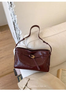 Detailed shot of oxblood leather shoulder bag with gold metal buckle on a cozy sofa