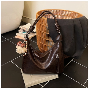 Détail du sac hobo en cuir marron foncé avec bandoulière nouée et breloque ours en peluche