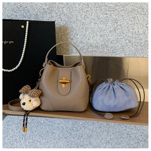 Detailaufnahme der beigen Eimer-Tasche mit goldenem Drehverschluss und Teddy-Anhänger