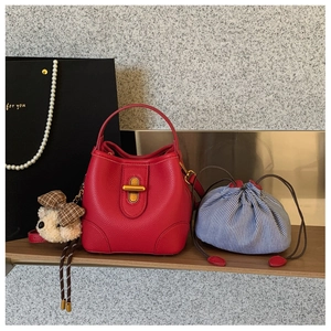 Details einer roten Eimertasche aus Kieselleder mit Goldschließe und Bärenanhänger