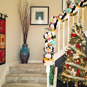 Pingüinos navideños de felpa con bufandas y gorros tejidos en barandilla de escalera