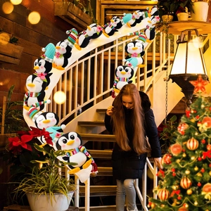 Peluche de pingüino con gorros y bufandas de colores en una escalera decorada de Navidad