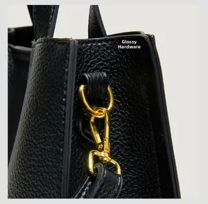 Detailed macro of black lychee grain leather and polished gold hardware of tote bag