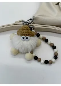 Detail of cute plush doll pendant with beads and lobster clasp on a leather bag