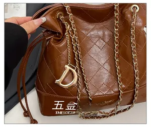 Detail of brown quilted bucket bag with gold D-charm and chain strap texture