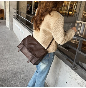 Detail of a large vintage dark brown leather messenger bag worn on a shoulder in the city