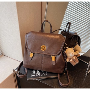 Detail of dark brown leather backpack with gold clasp and cute teddy bear charm