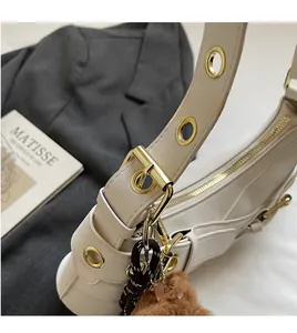 Detail of beige hobo bag with large gold eyelet strap and cute bear charm pendant