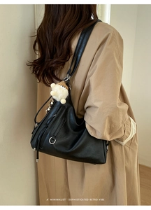 Minimalist black faux leather tote with decorative zipper, tassel detail and plush charm