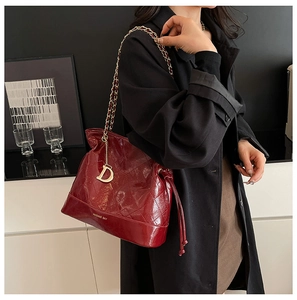 Close-up of red quilted bucket bag with gold metal chain and decorative letter D charm