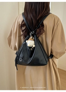 Detail of a black leather backpack featuring a white plush toy charm and silver metal ring
