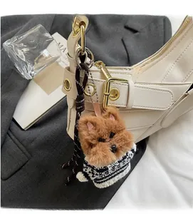 Brown plush puppy charm wearing a striped sweater on a white leather handbag