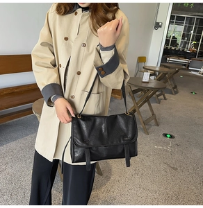 Detail of a vintage black leather crossbody bag with decorative straps on a beige trench coat