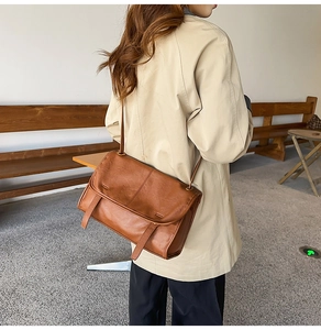 Brown vintage leather messenger bag styled with a beige trench coat in a cafe setting