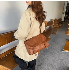 Brown vintage leather messenger bag worn with a beige coat in a lifestyle setting
