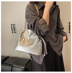 Detail view of silver quilted bucket bag featuring a D-charm and gold-toned metal chain strap