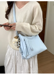 Detail of light blue crossbody bag featuring long tassels and unique gnome bead charm