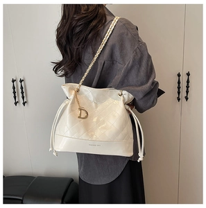 Detailed view of white quilted bucket bag with gold chain strap and metal letter charm