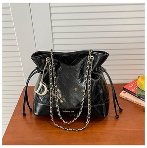 Detailed view of black quilted bucket bag with chain strap and gold letter pendant