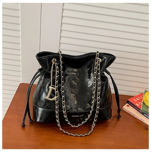 Detail of black glossy quilted bucket bag with gold chain strap and D-shaped charm