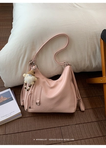 Detailed view of pink leather hobo bag with plush doll charm on wooden floor