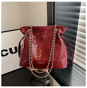 Detailed view of dark red quilted bucket bag with gold chain and D-shaped metal pendant