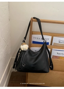 Detail of a black leather hobo tote bag featuring a tassel zipper and white plush charm