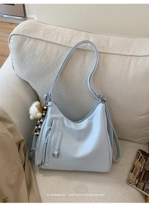 Detail of light blue faux leather shoulder bag with plush lamb charm on a soft sofa