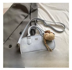Sac bowling en cuir bleu clair avec breloque ours posé sur une veste grise chic