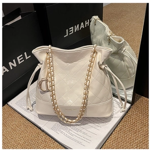 Detail of cream bucket bag with quilted patterns, golden chain, and metallic charm
